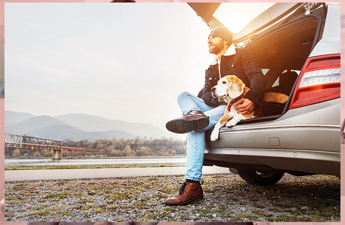 breaded man siting in car trunk enjoying weather with pet